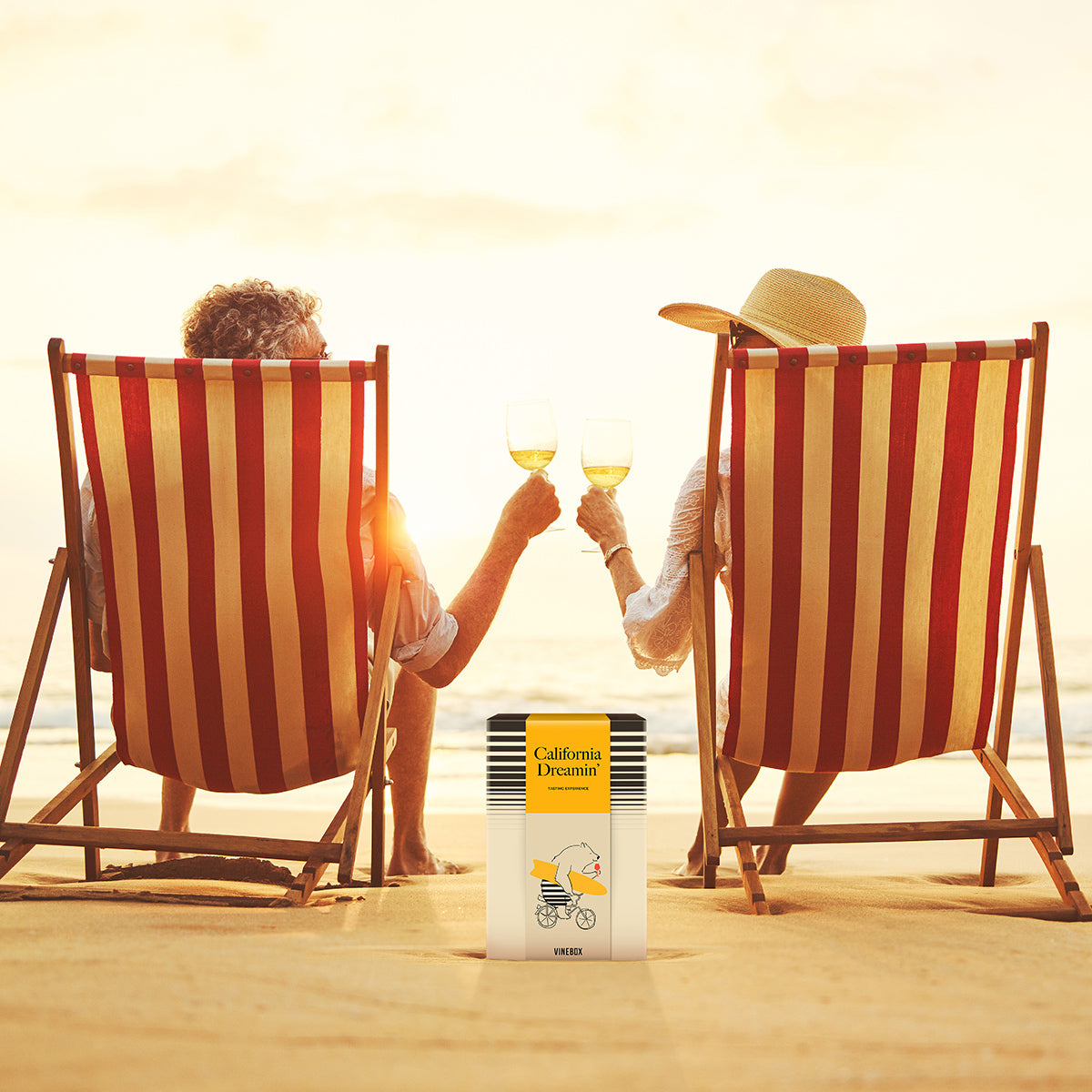 Two people sitting on striped beach chairs at sunset, clinking glasses with a 'California Dreamin'' product in the foreground.