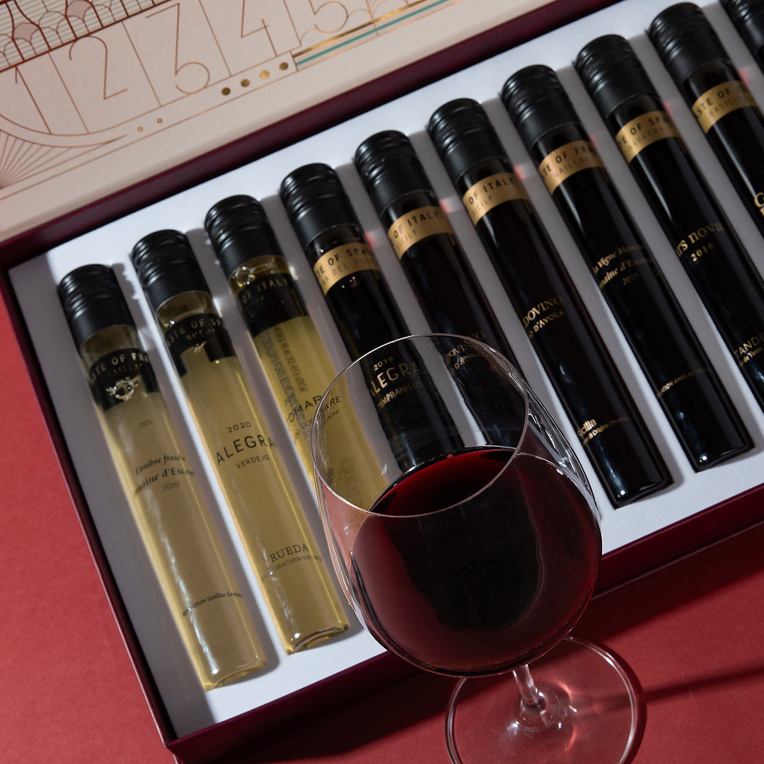 Set of wine bottles in a box with a glass of red wine in front