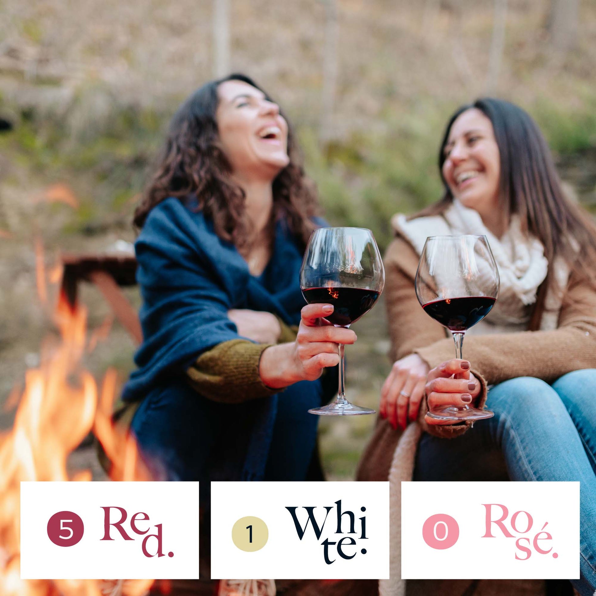 Two women sitting by a campfire holding wine glasses