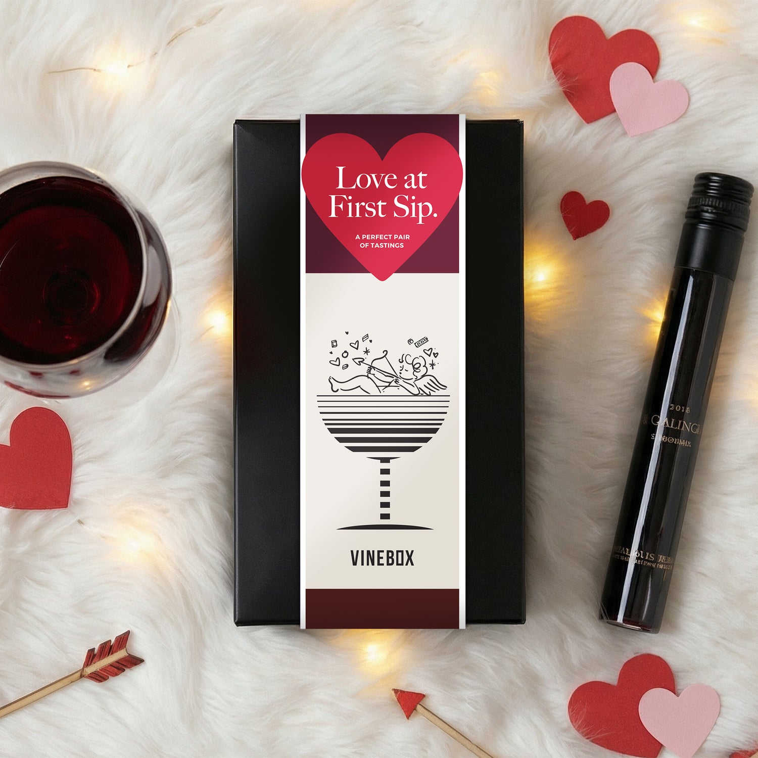 Vinebox packaging with a glass of red wine, bottle, and heart decorations on a soft surface.